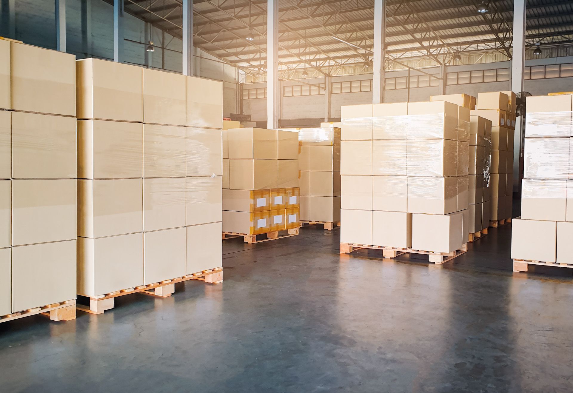 A warehouse filled with lots of cardboard boxes on wooden pallets.