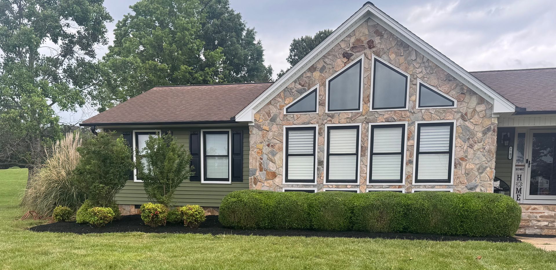 Single-story brick house with a large triangular front window, white trim, and a manicured hedge