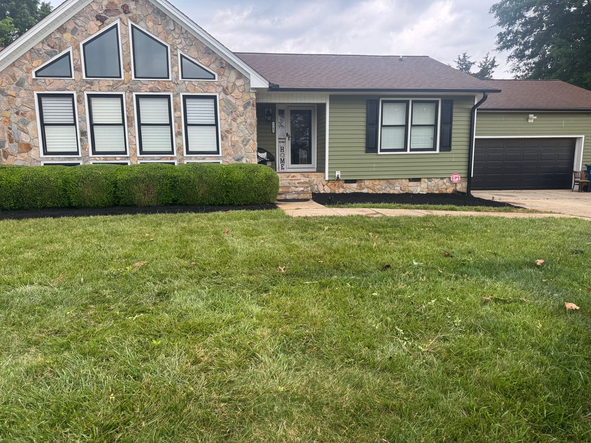 Single-story house with stone and green siding, front lawn, and attached garage