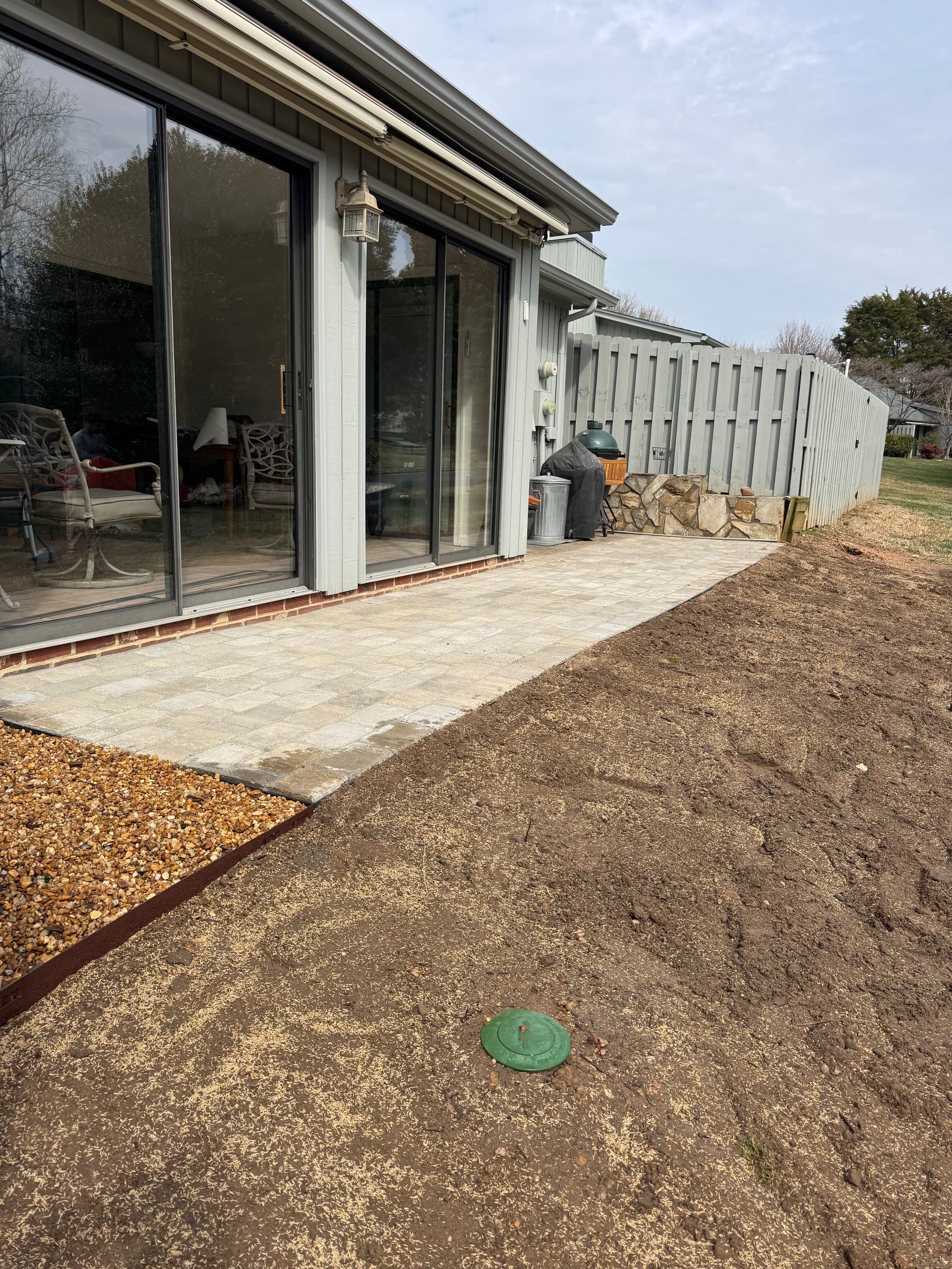 Backyard patio with sliding glass doors, concrete path, gravel yard, and a white fence under clear sky