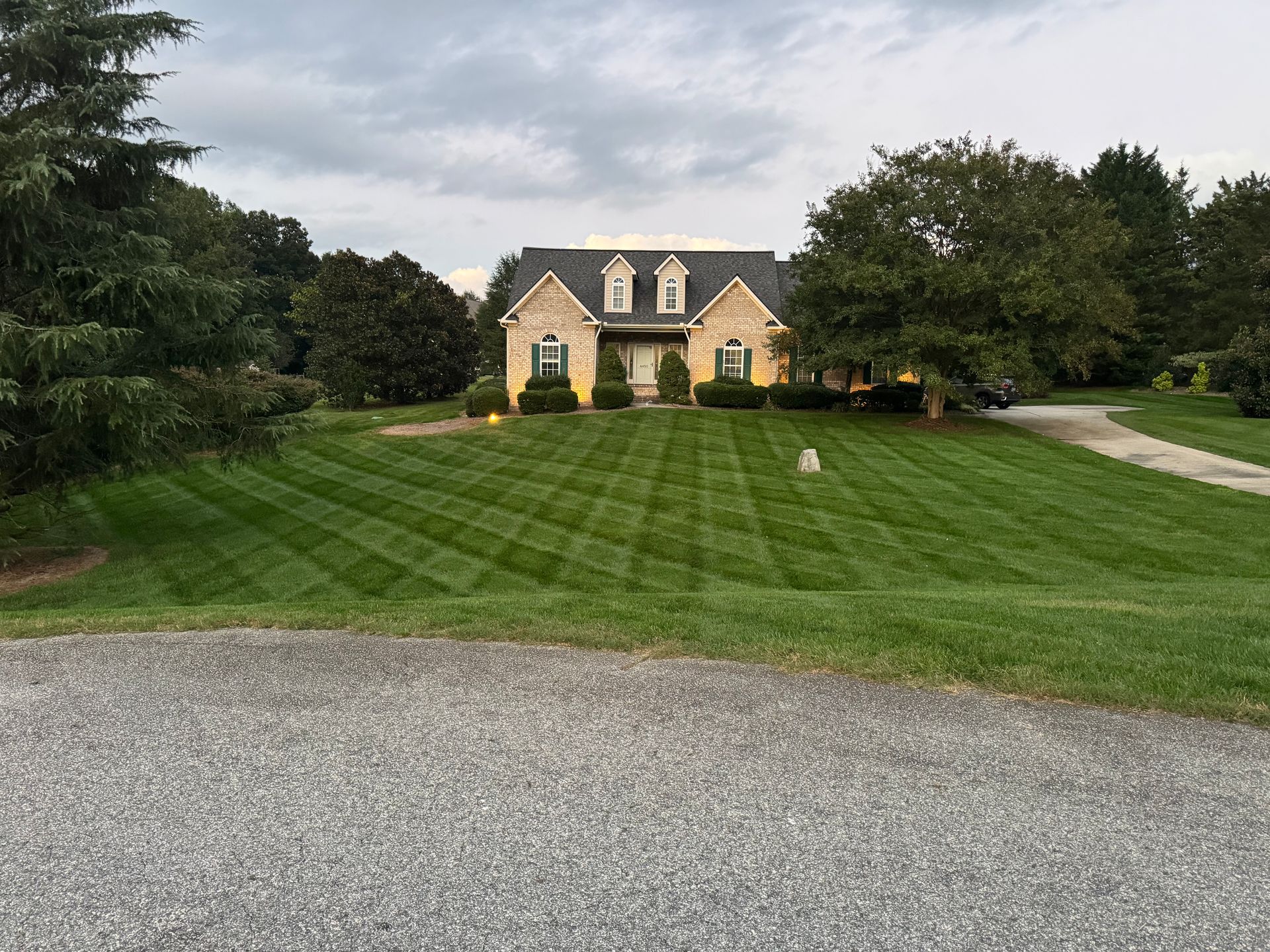 Large yellow house with a manicured lawn, gravel driveway, and trees in front