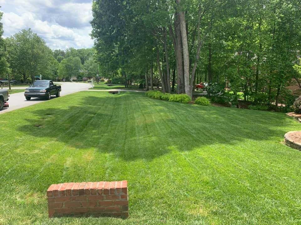 Suburban lawn with striped grass, brick mailbox, trees, and parked black truck by the road