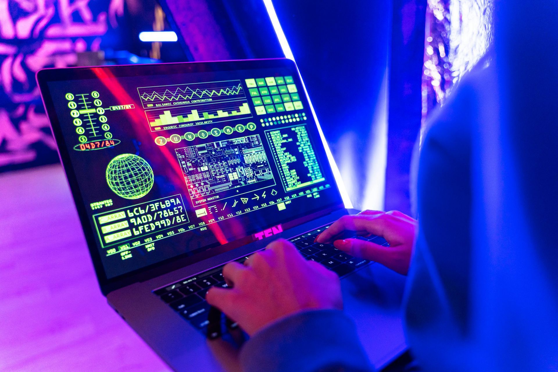 Person using laptop displaying complex technical data, illuminated by neon lights.