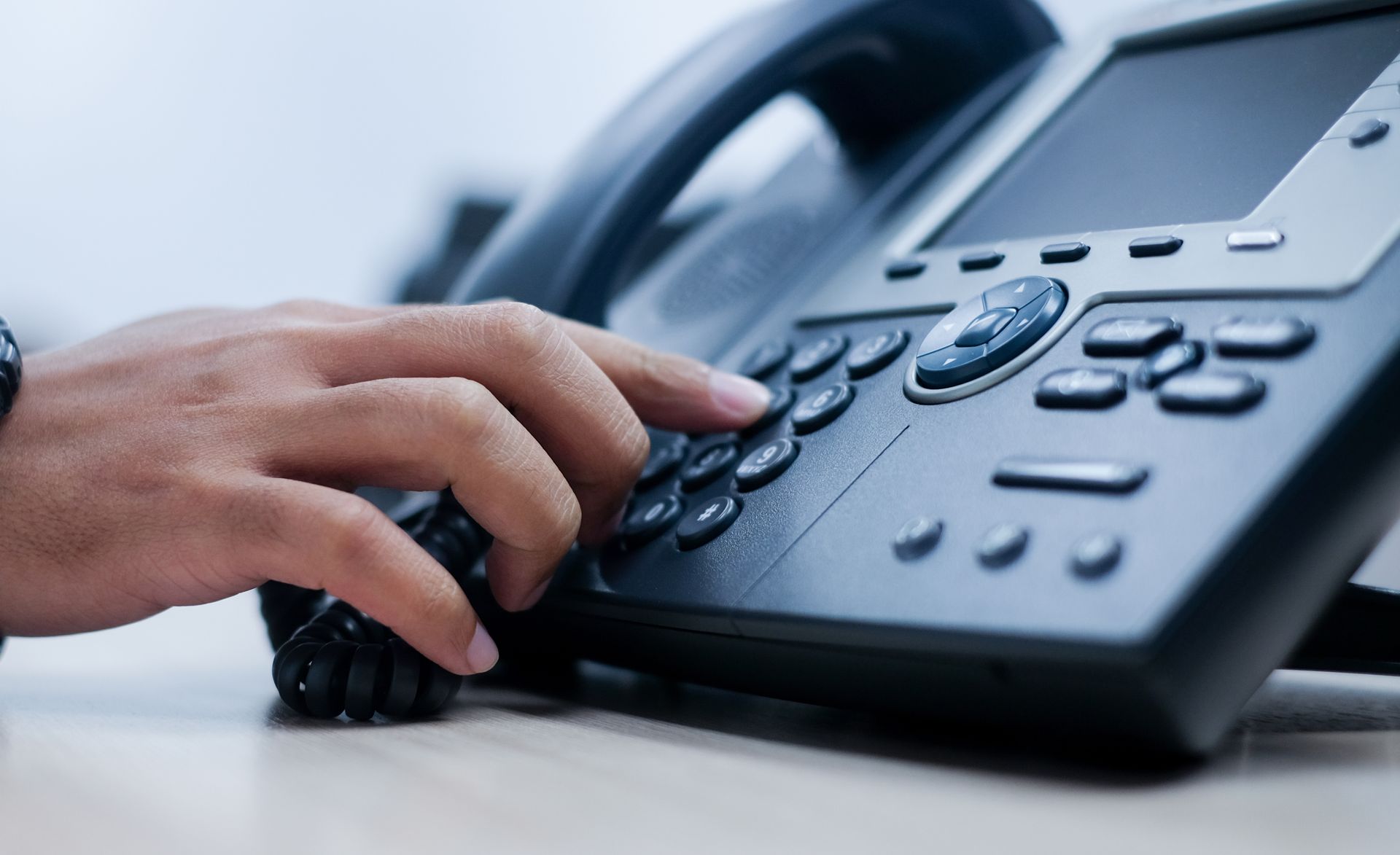 Hand dialing a phone on a desk in an office, pressing buttons on the phone's keypad.