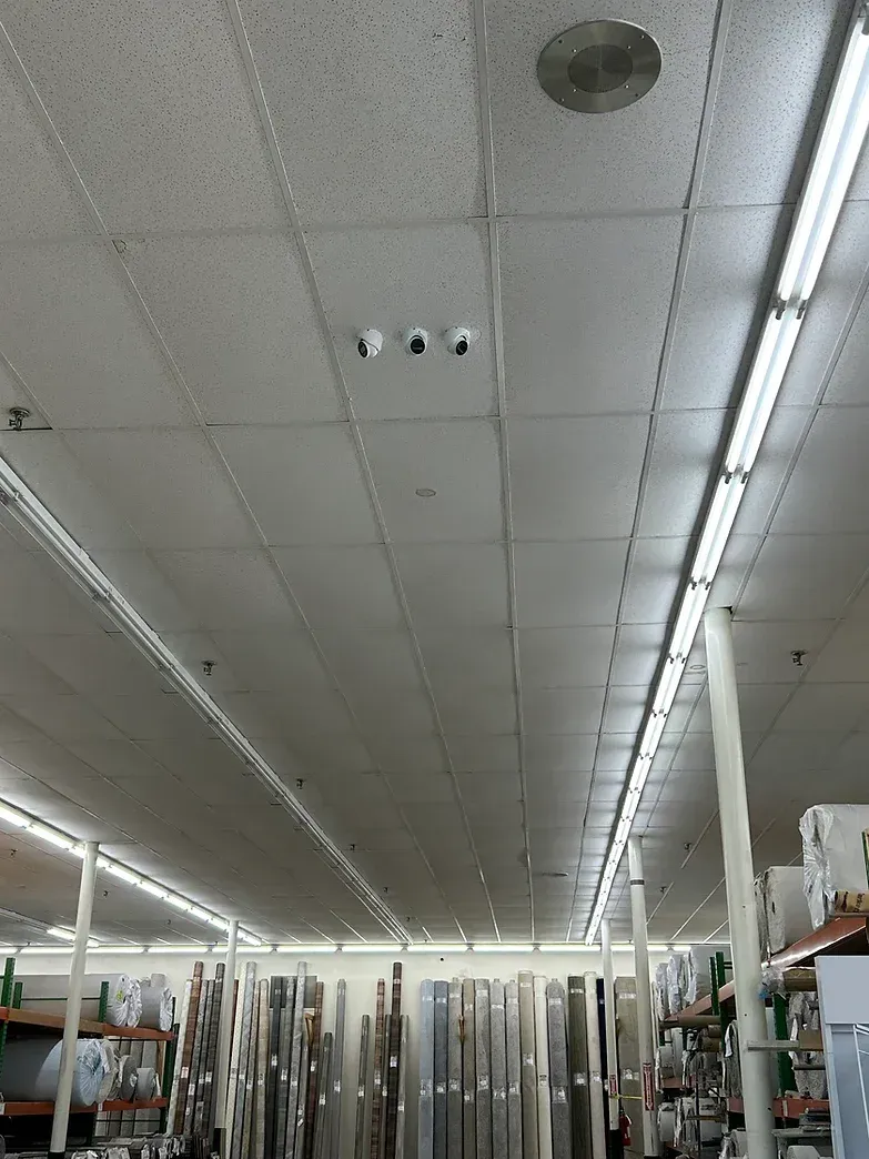 White ceiling with fluorescent lights and security cameras in a retail store.