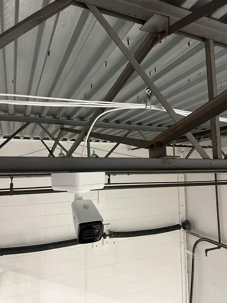 Security camera mounted on a metal beam ceiling with conduit and a fluorescent light.