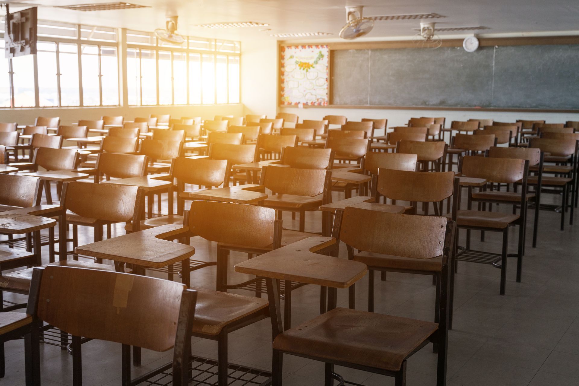 An empty classroom with rows of wooden desks and chairs.