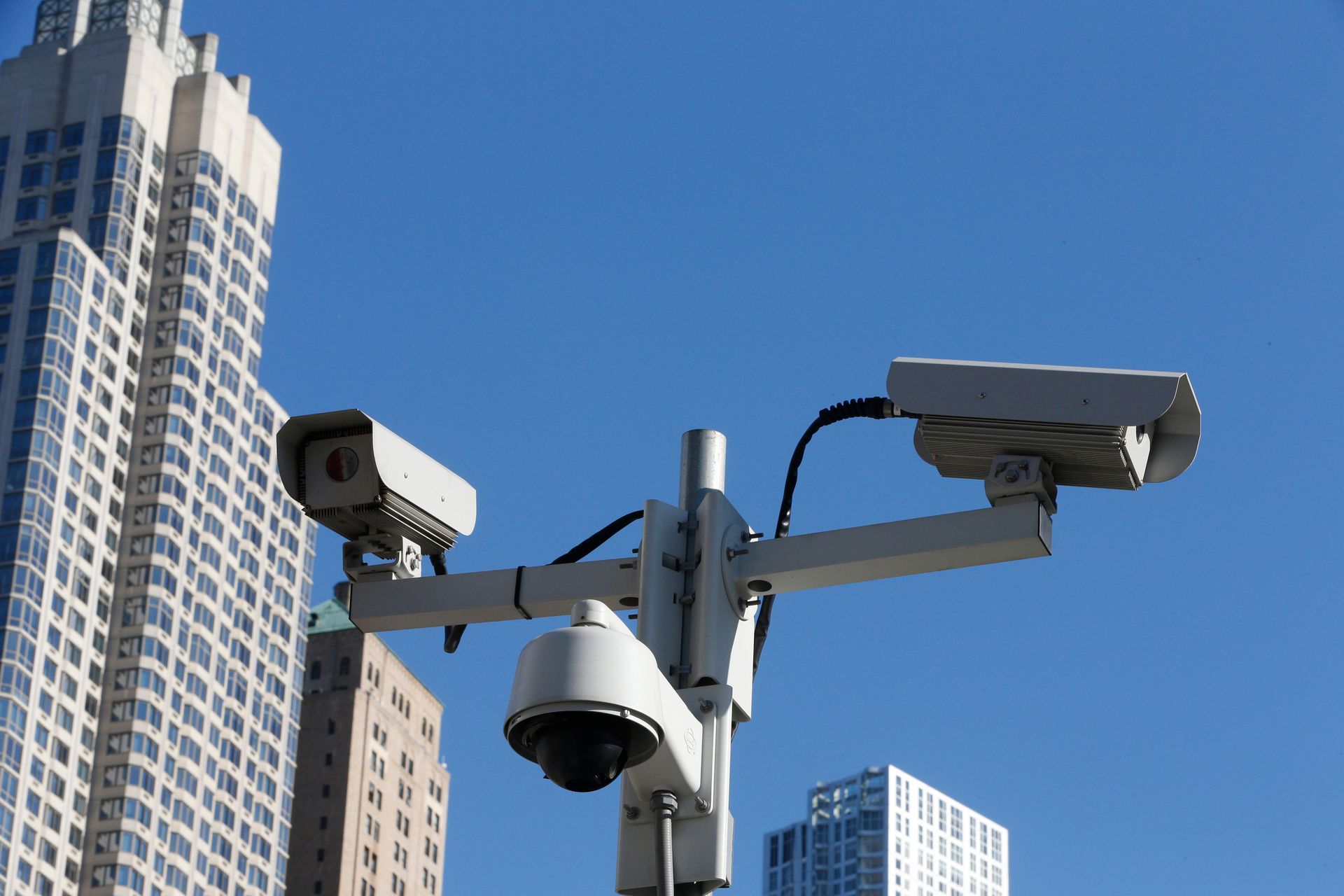 Two security cameras are sitting on a pole in front of a tall building.