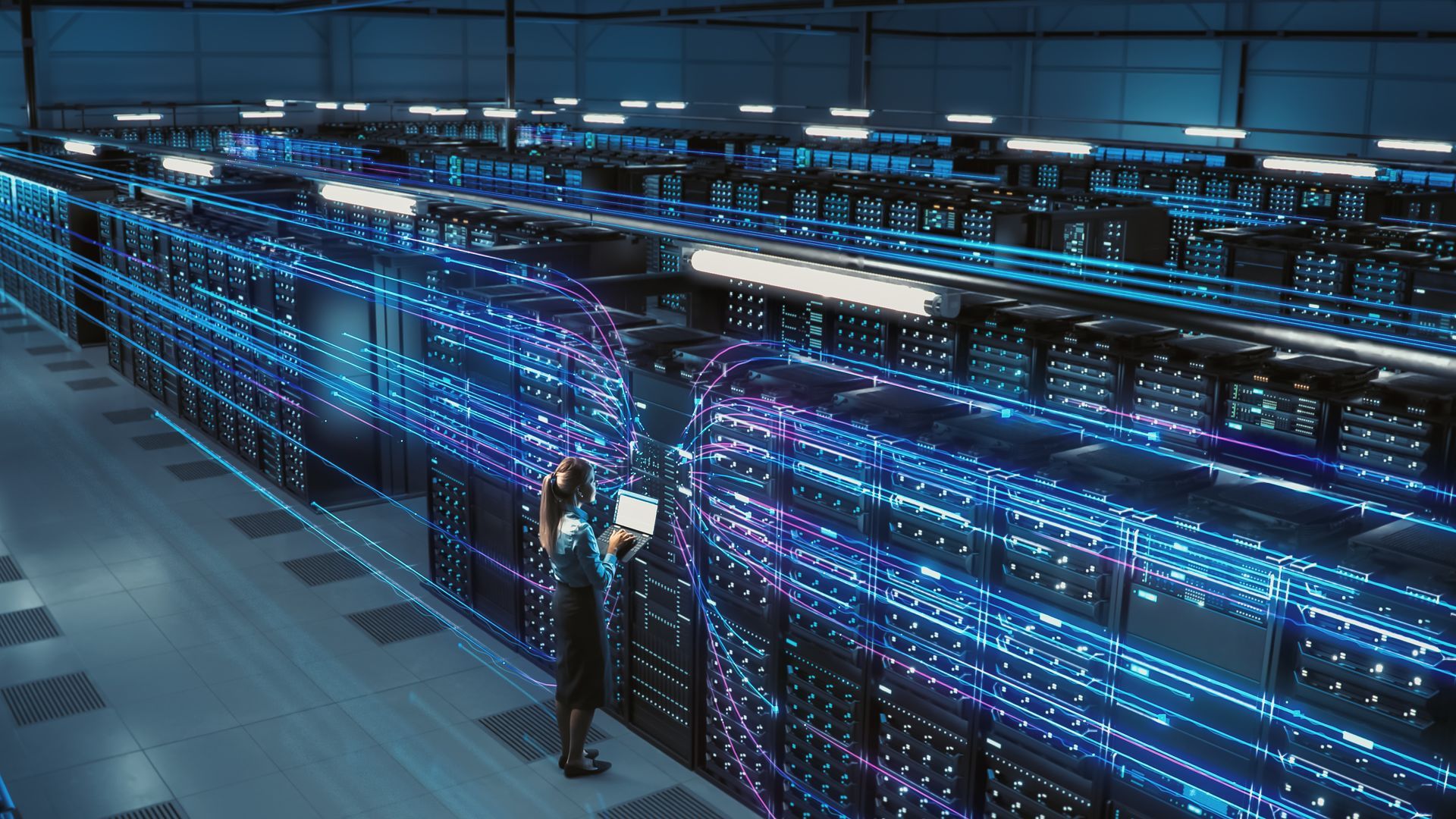 A man is standing in a data center looking at a tablet.