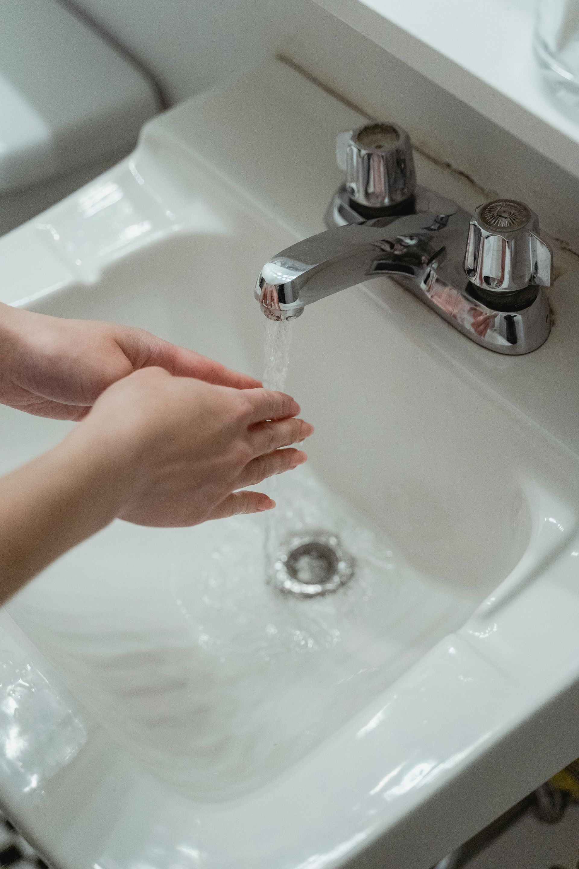 Person washing hands under running water in a white sink.