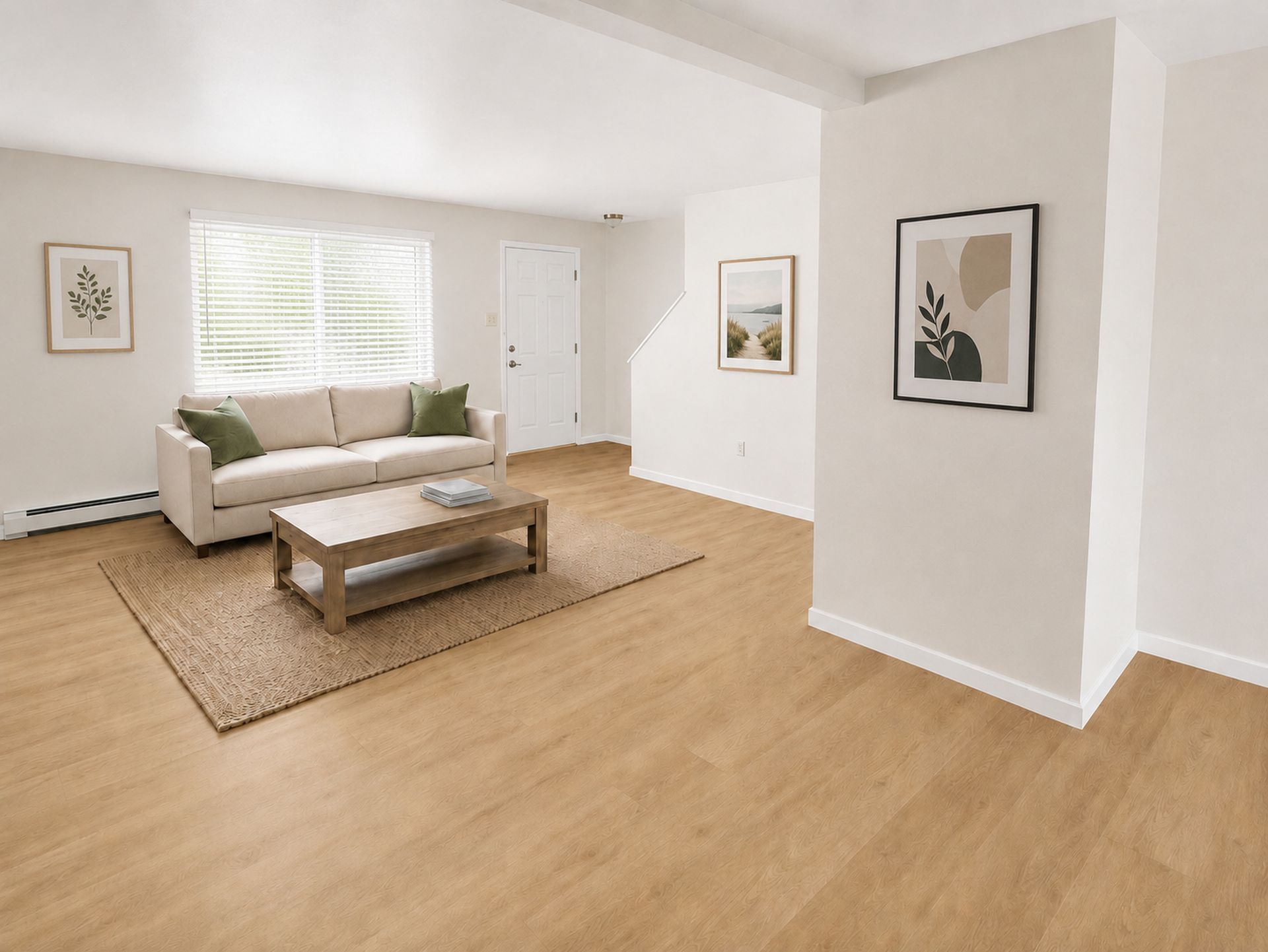 Bright living room with white walls, light wood floors, beige sofa, coffee table, and framed wall art.