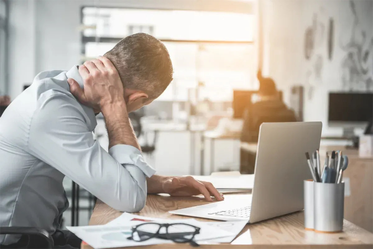 Man at desk with laptop, holding neck in pain, office setting — Bespoke Legal Group In Northern, NSW