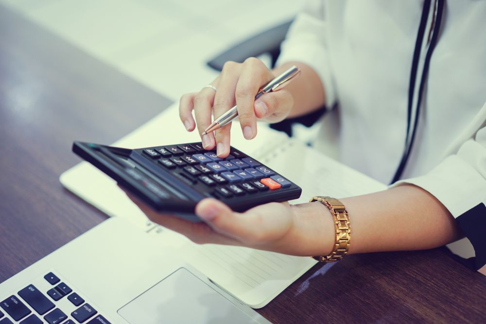 Person using a calculator, holding a pen, and working on a notebook — Bespoke Legal Group In Southport, QLD