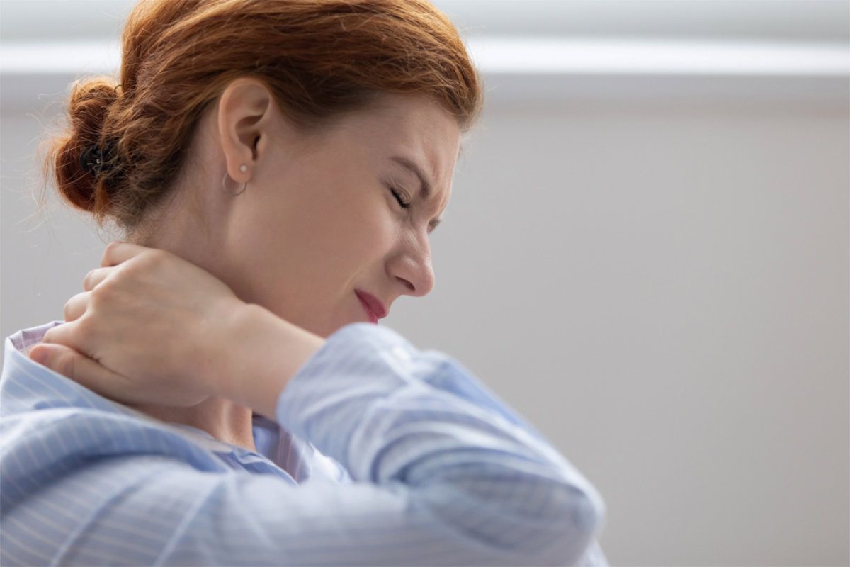 Woman with red hair, in light blue shirt, holding neck in pain. Eyes closed, likely indoors — Bespoke Legal Group In Southport, QLD