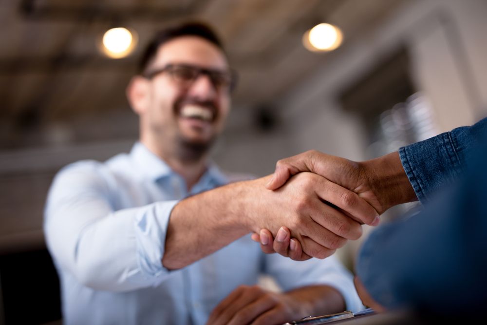 Man in glasses smiles, shaking hands with another person, light blue shirt. — Bespoke Legal Group In Southport, QLD