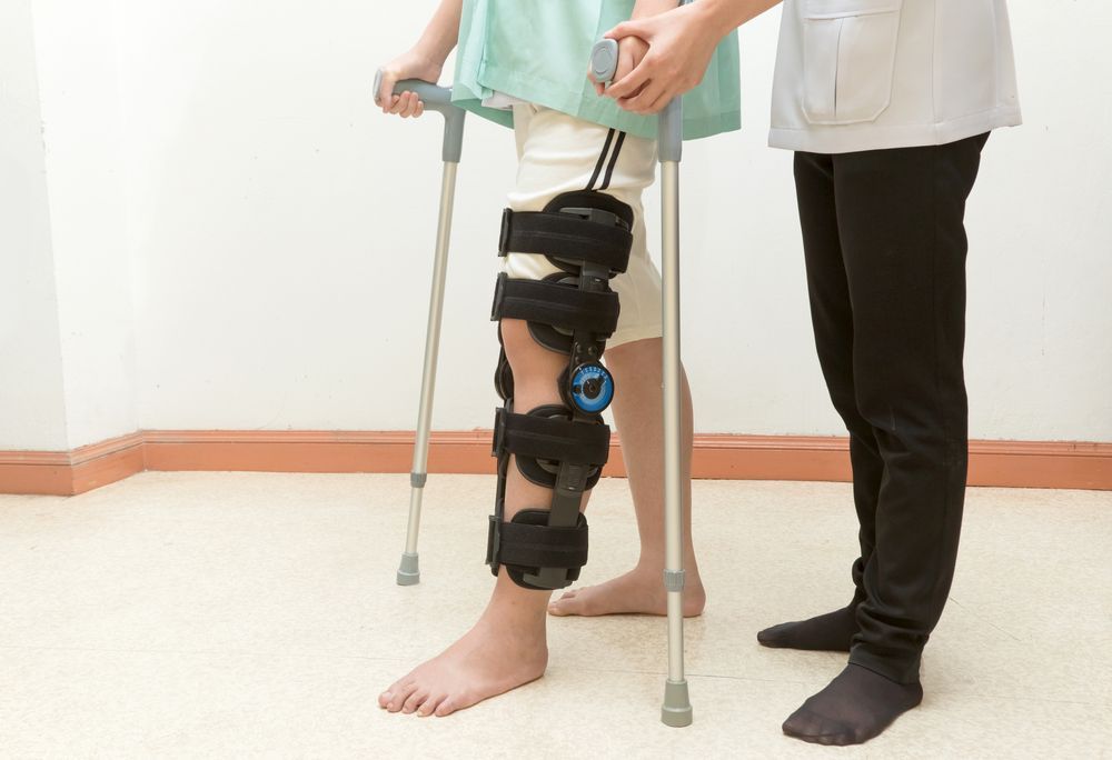 Person with a leg brace using crutches, assisted by another person indoors - Bespoke Legal Group In Southport, QLD