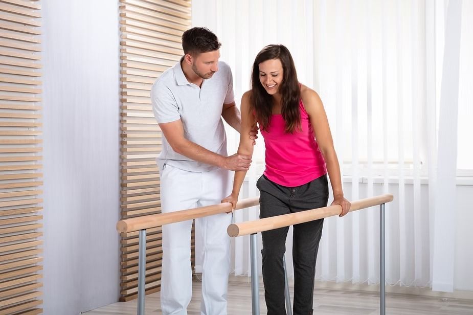 Physical Therapist Assists a Woman Walking Between Parallel Bars in a Bright Room — In Southport, QLD