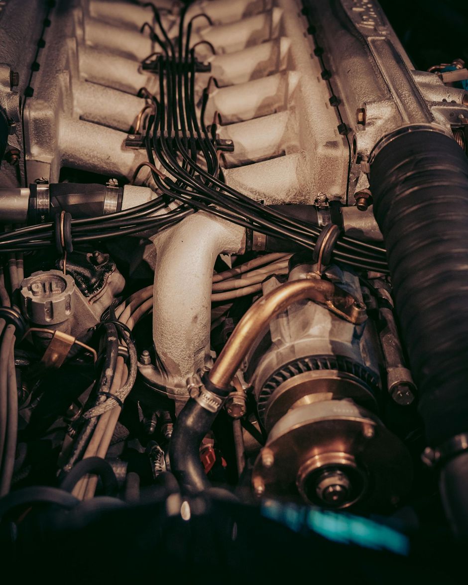 Close-up of a car engine with visible components, including wiring, hoses, and metal parts.