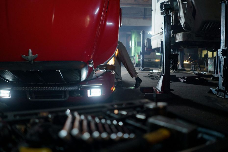 Mechanic under a red truck in a garage, tools in foreground.