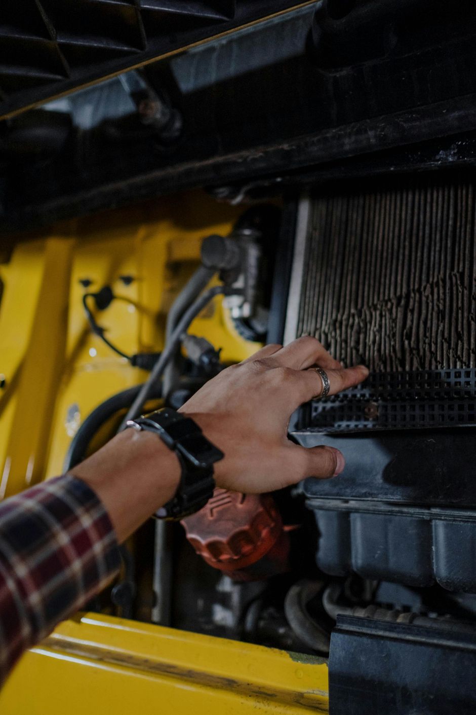 Hand examining a dirty air filter in a yellow vehicle's engine compartment.