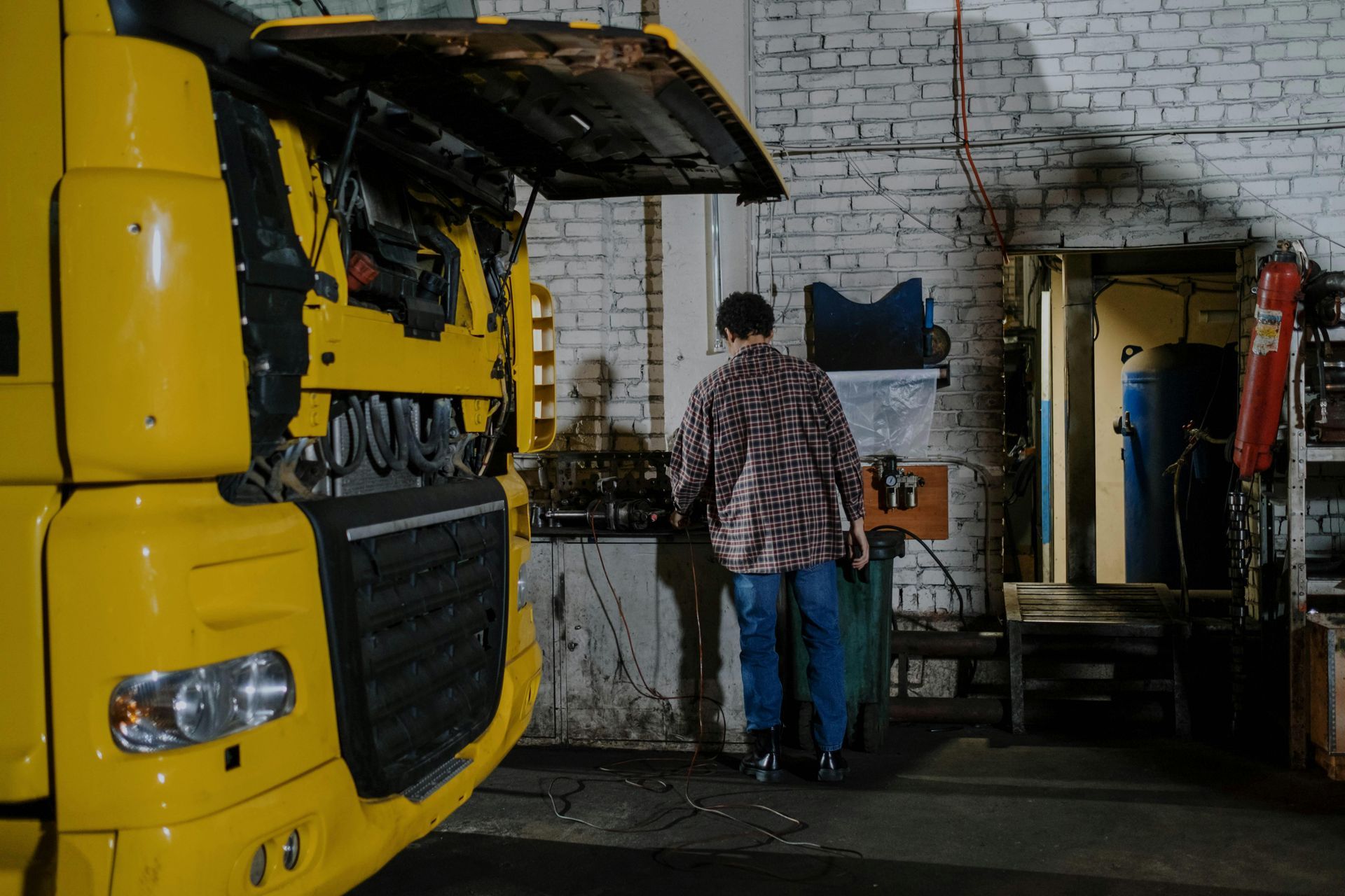 Yellow truck with open hood, person in a garage.