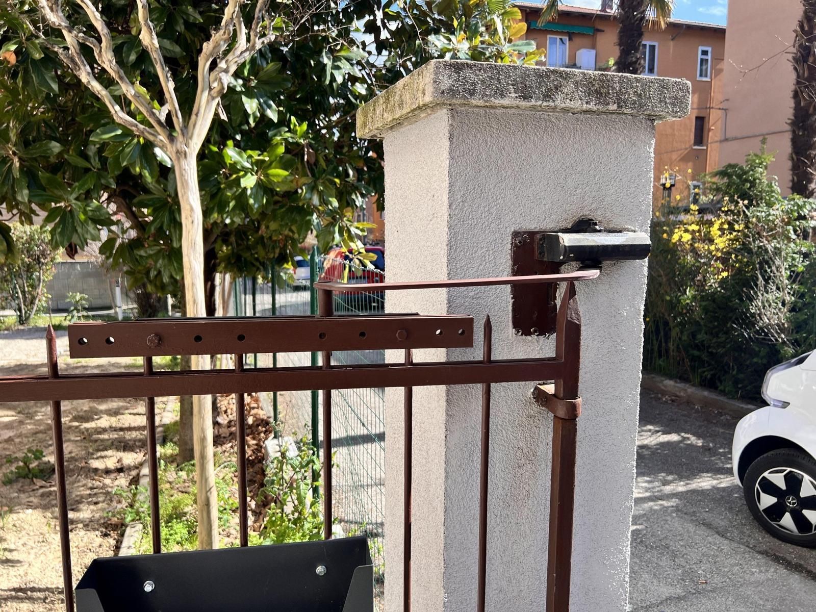 Cancello di metallo arrugginito accanto a un pilastro di stucco bianco in una soleggiata strada residenziale