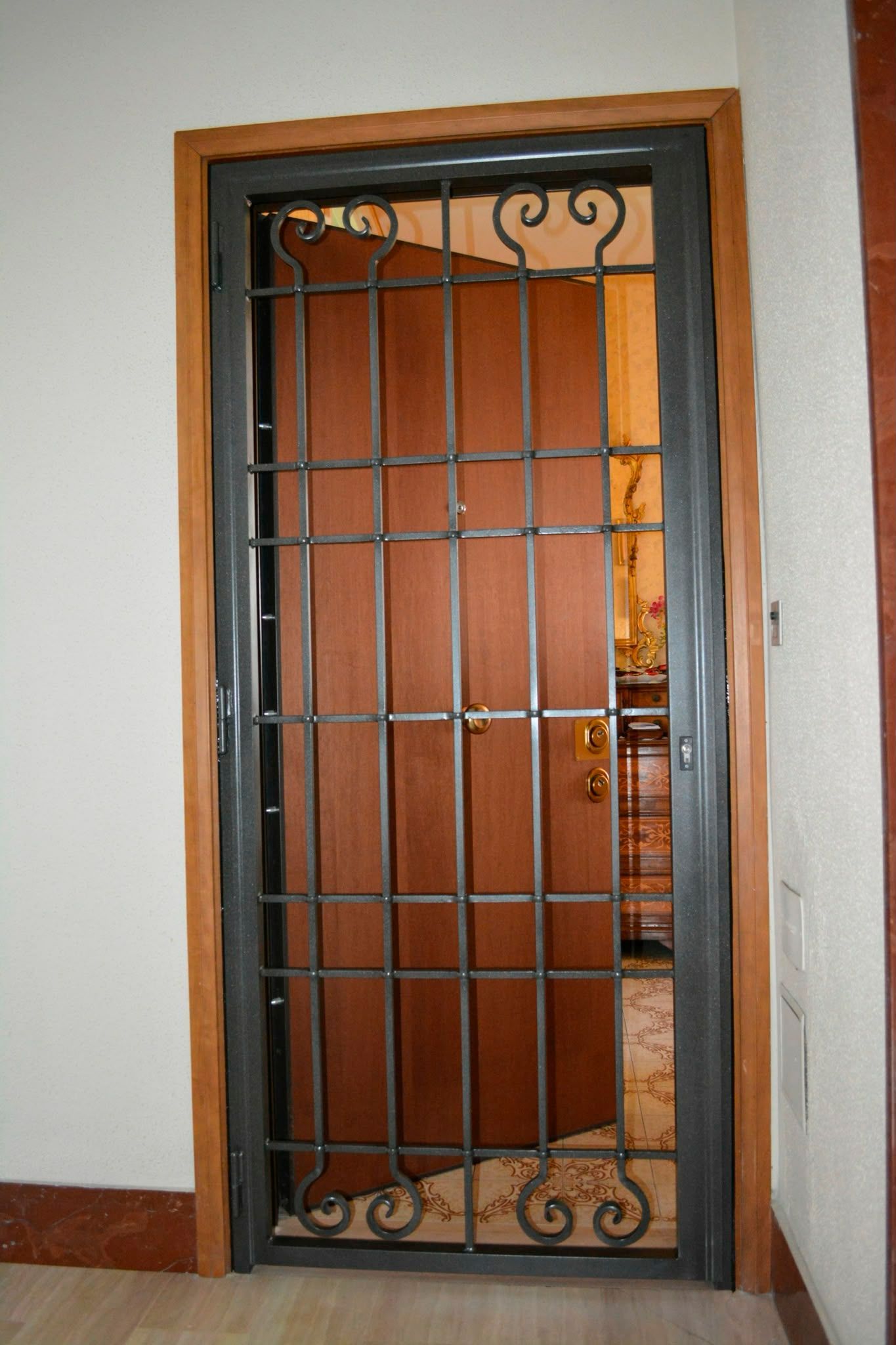 Cancello di sicurezza in metallo davanti a una porta di legno di un appartamento, con un muro arancione alle spalle.