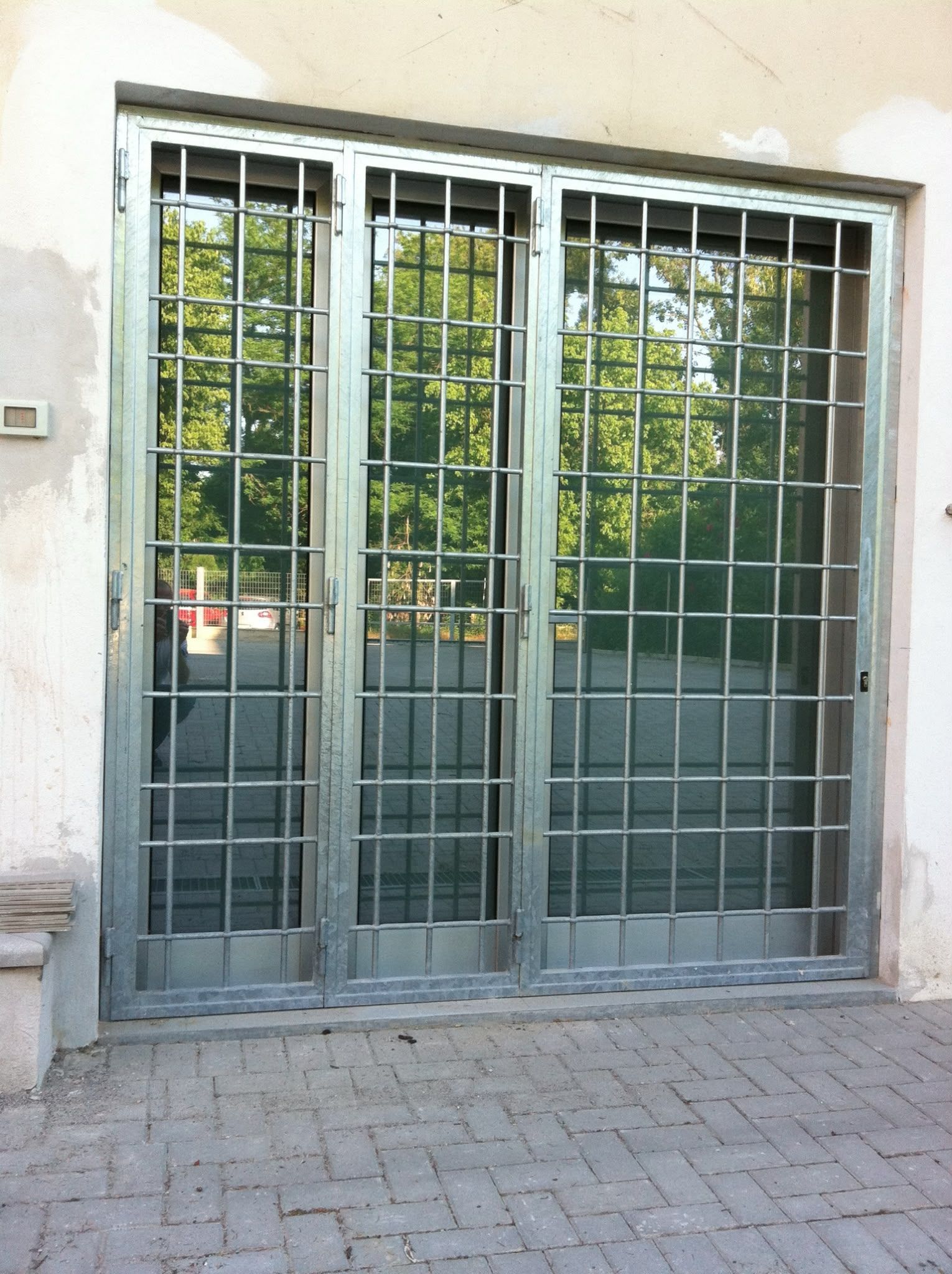 Ingresso con facciata in vetro, grate di sicurezza in metallo e vialetto pavimentato antistante.