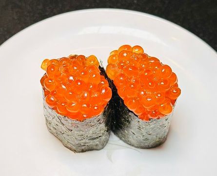 Two sushi rolls topped with bright orange salmon roe on a white plate