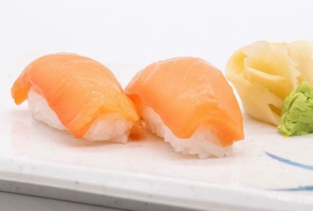 Two salmon nigiri sushi pieces with pickled ginger and wasabi on a white plate