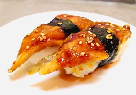 Glazed grilled fish sushi with sesame seeds on a white plate