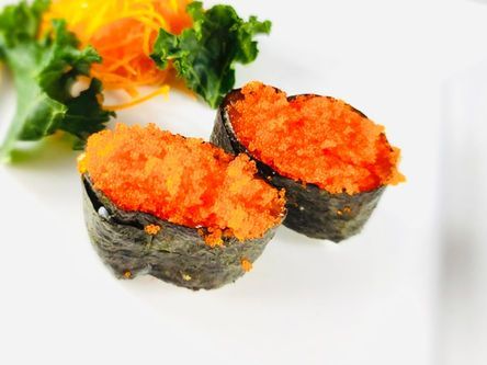 Sushi rolls topped with bright orange fish roe on a white plate, garnished with greens and sliced carrot curls