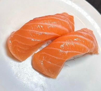 Two pieces of raw salmon sushi on a white plate