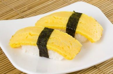 Two pieces of tamago sushi with black seaweed strips on a white plate