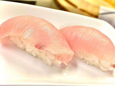 Two pieces of pale pink nigiri sushi on a white plate, close-up view