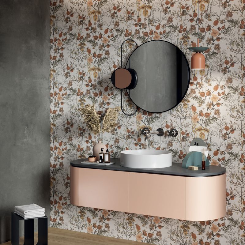 Bagno con carta da parati floreale, specchio rotondo, mobile lavabo in rame e lavabo bianco.