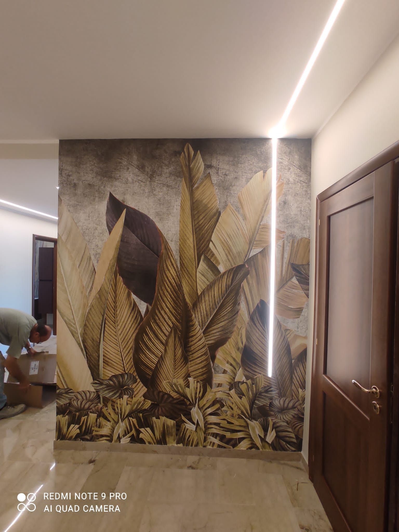 Corridoio con carta da parati con foglie tropicali, illuminazione lineare da incasso e porta marrone.