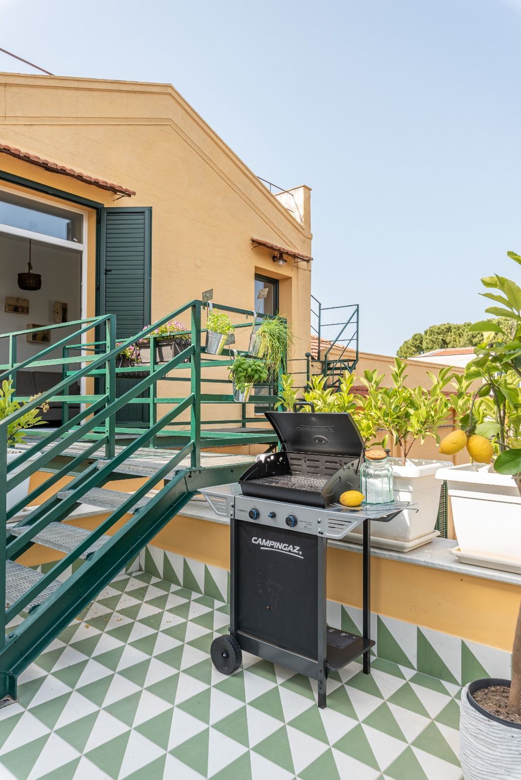 Griglia a gas su un patio sul tetto con scale verdi e alberi di limone.