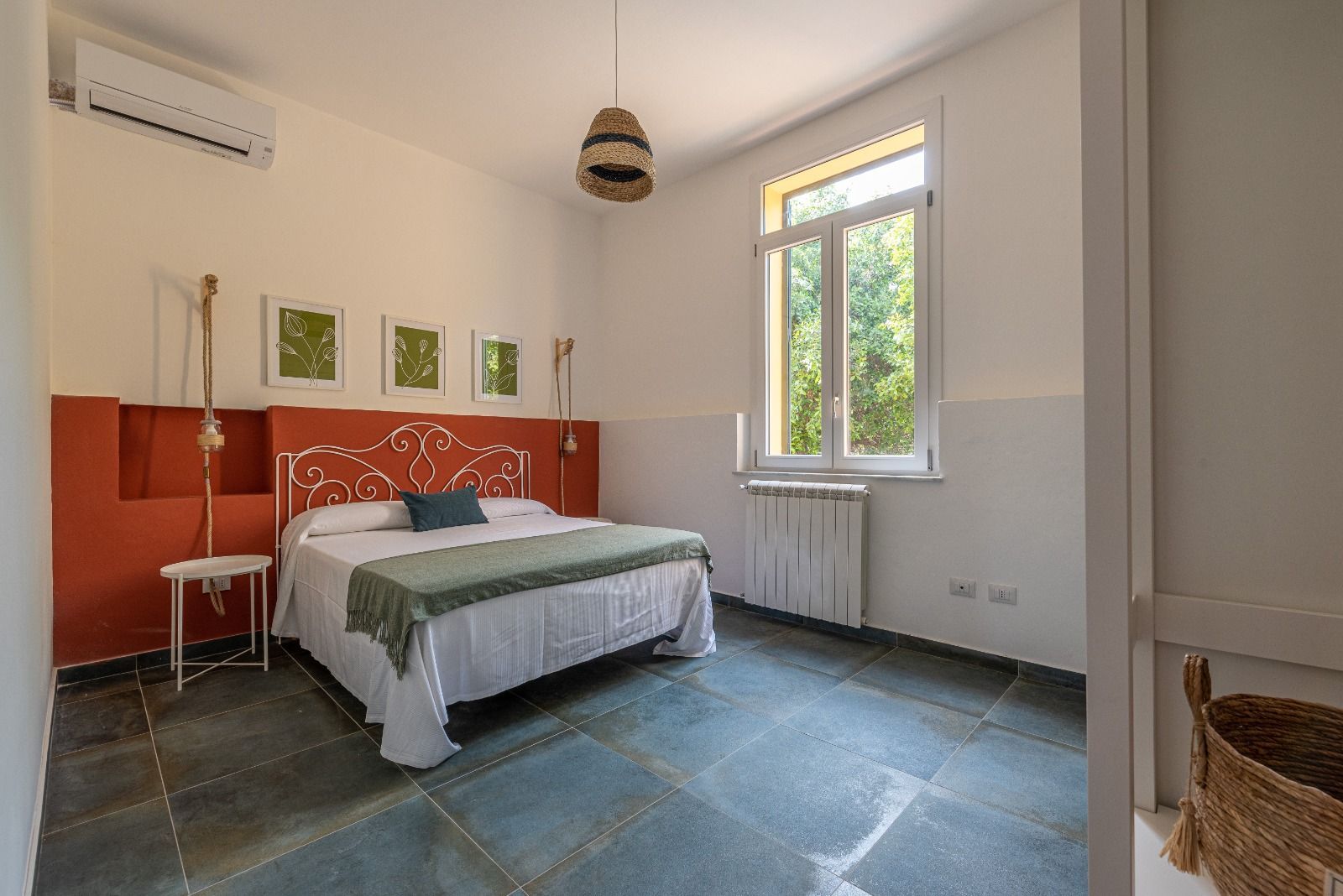 Camera da letto con letto, testiera arancione, tre stampe incorniciate, aria condizionata e finestra.