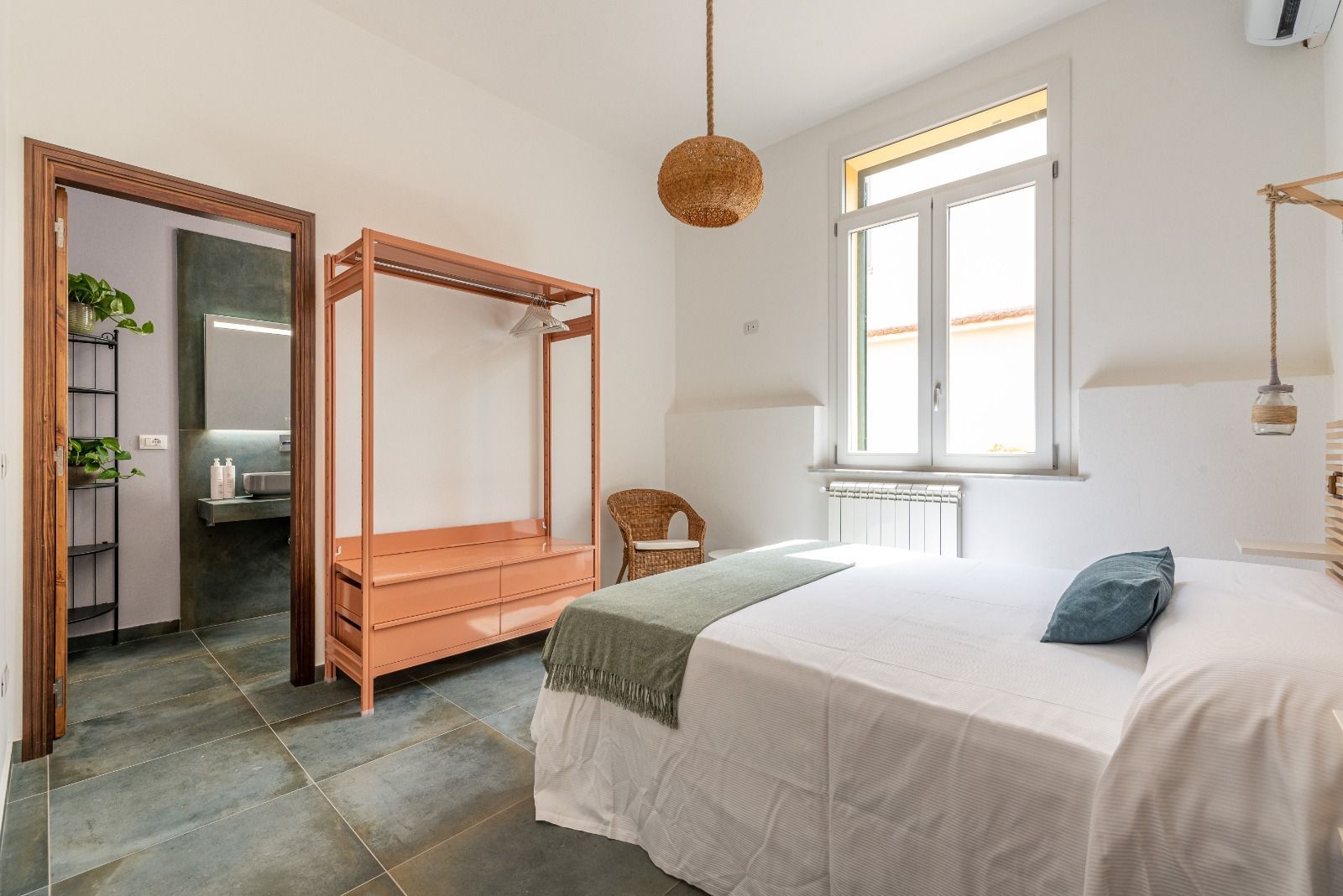 Camera da letto con letto a baldacchino, porta aperta sul bagno, pareti bianche, pavimento in pietra e finestra.