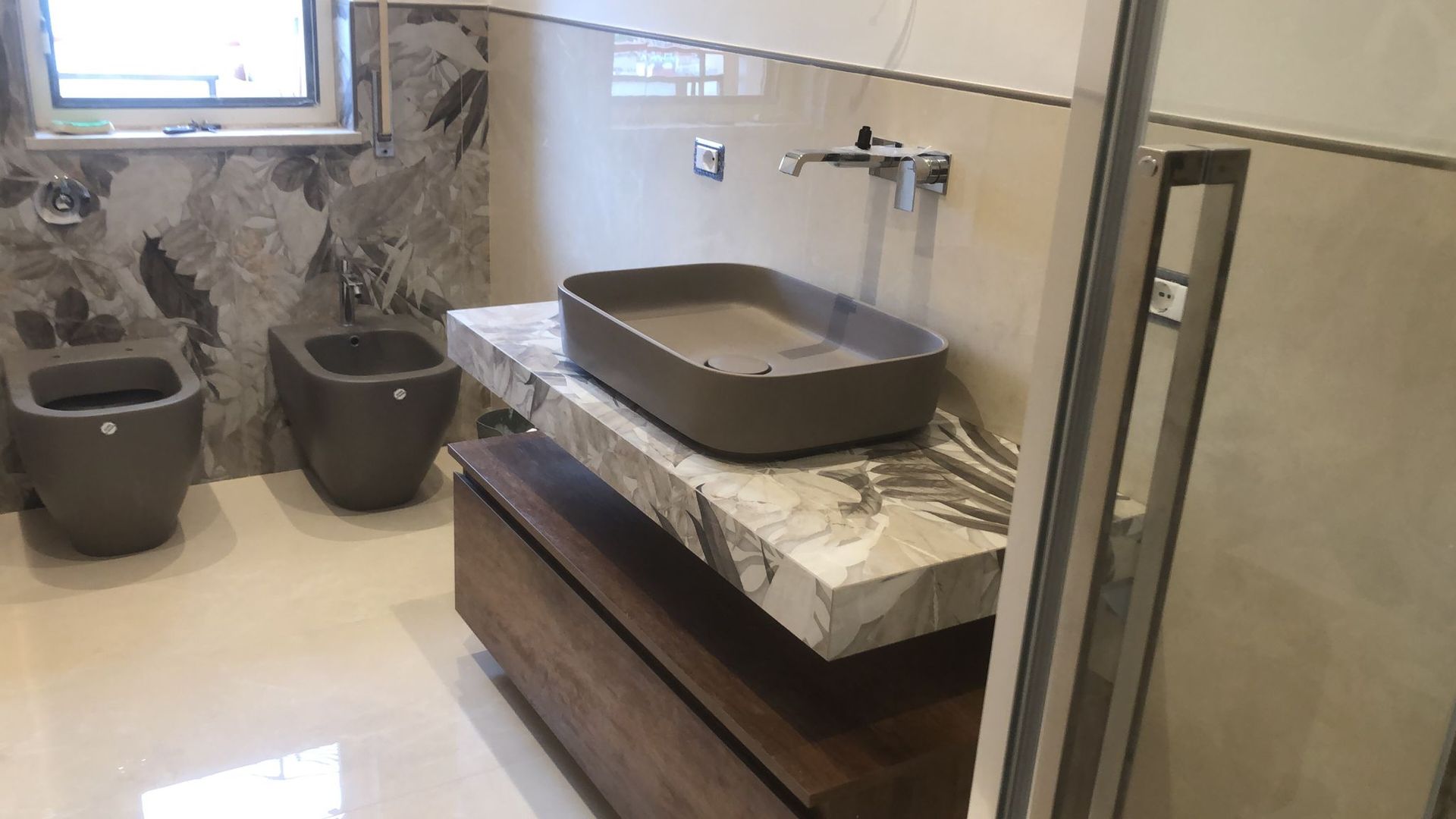Bagno moderno con sanitari grigi, piano di lavoro in marmo sospeso e mobiletto in legno.