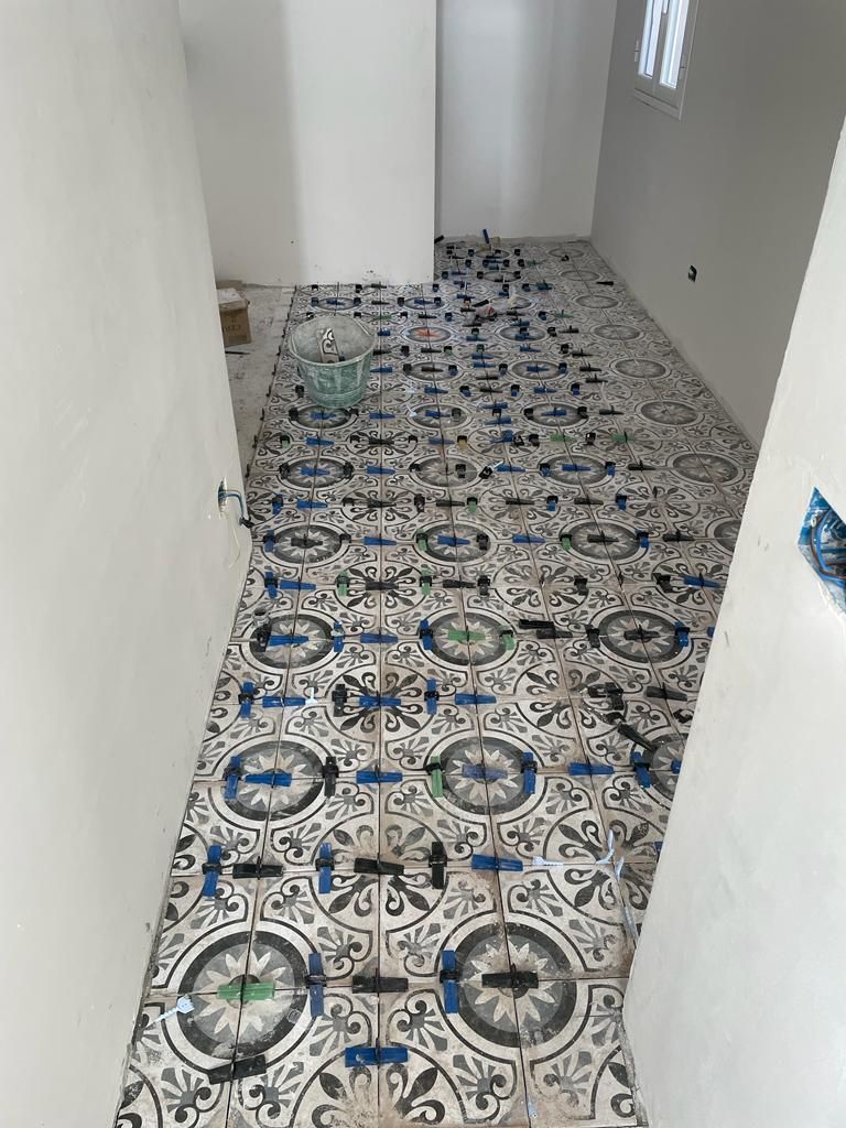Pavimento piastrellato di recente con piastrelle blu, grigie e bianche a motivi geometrici in una stanza con pareti bianche.