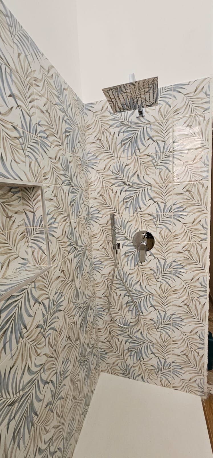 Doccia con piastrelle decorate, soffione e rubinetto su sfondo bianco.
