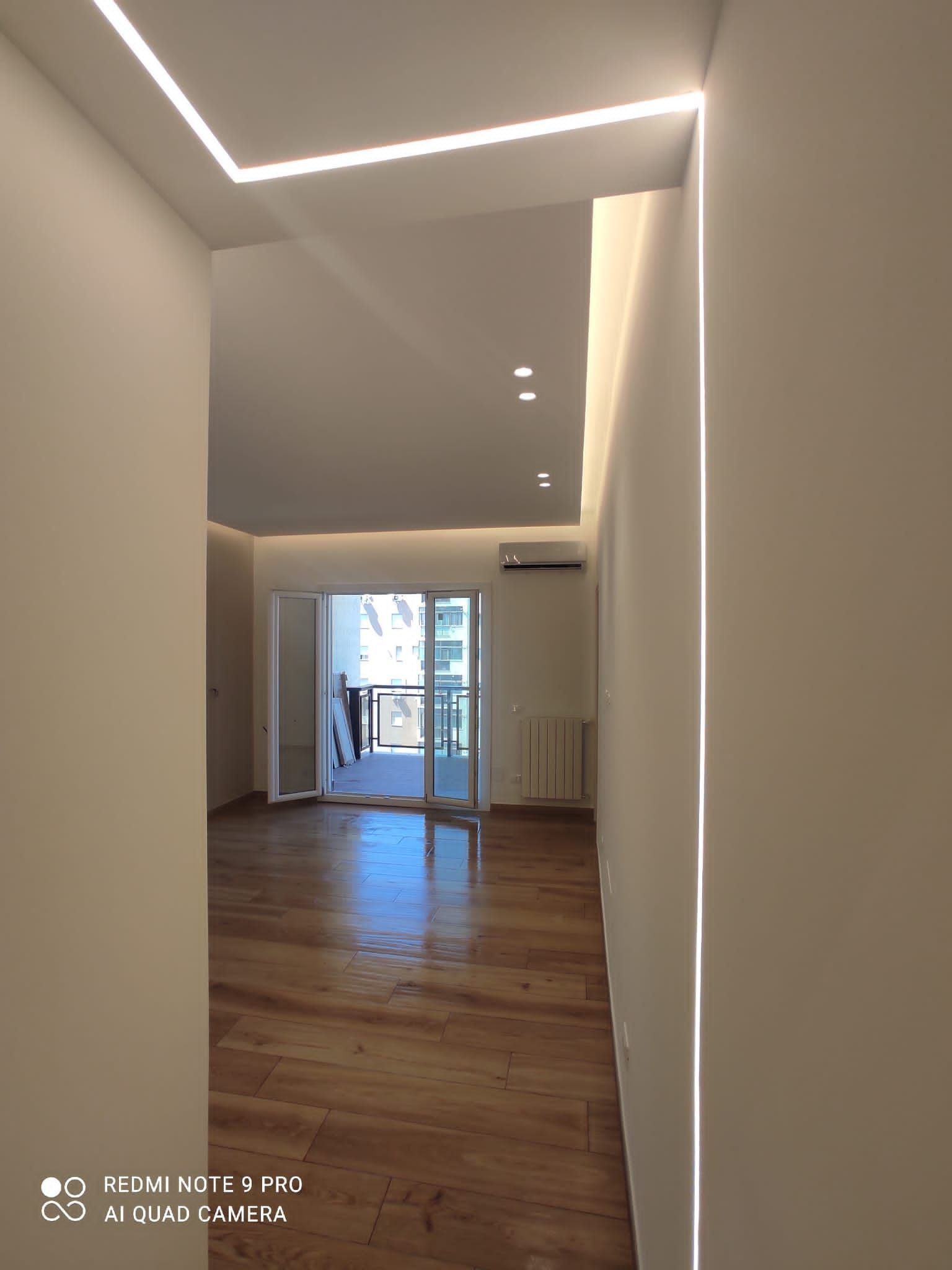 Corridoio stretto con pavimento in legno, illuminazione da incasso e porta che conduce a un balcone.