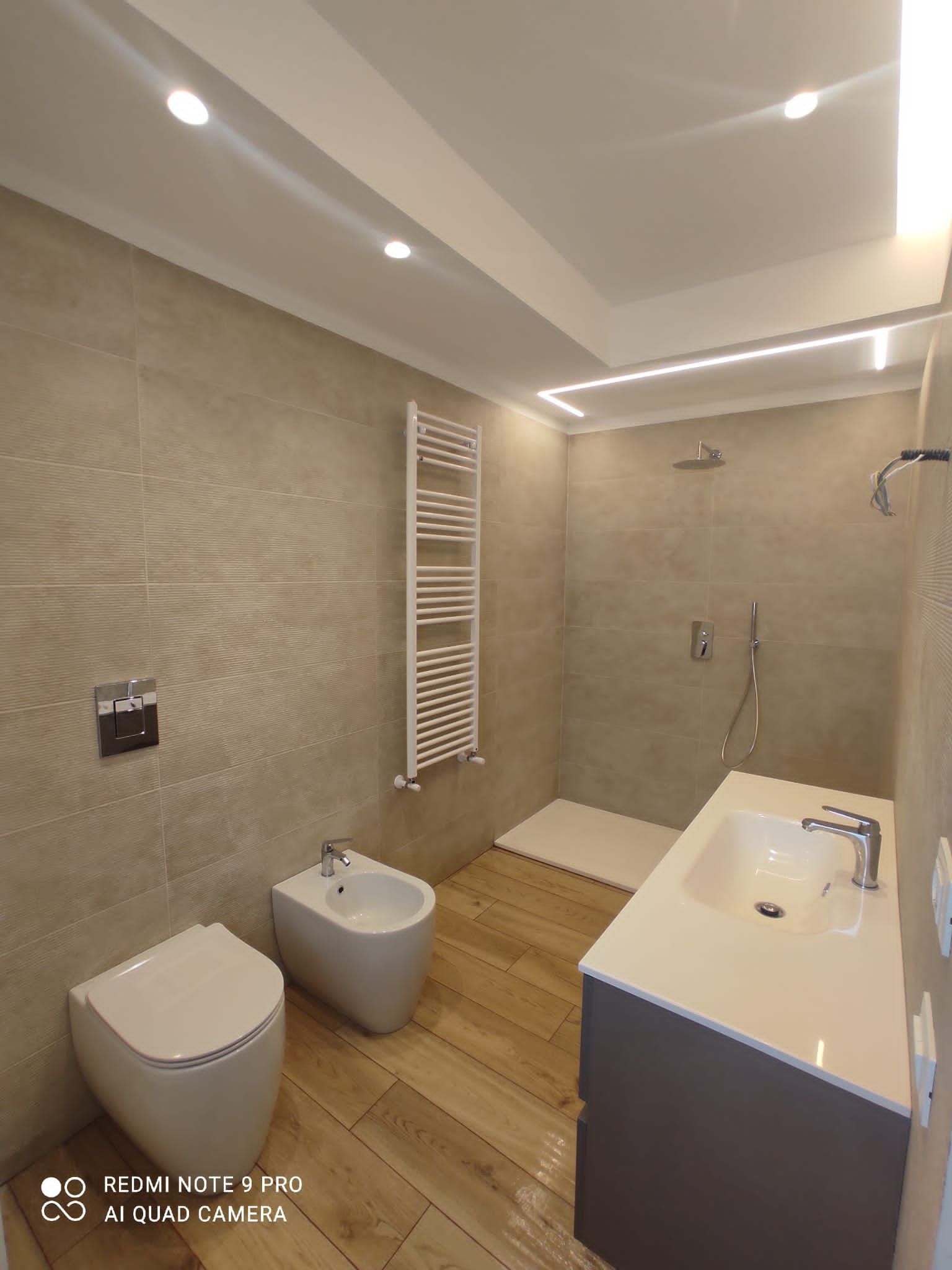 Bagno moderno con pareti color cuoio, pavimento in legno, sanitari bianchi e doccia.