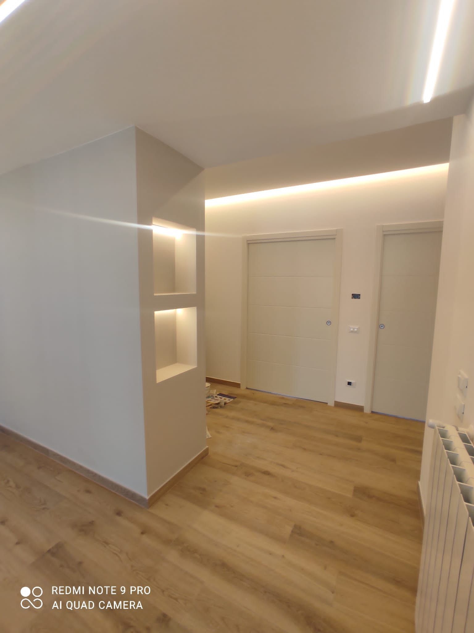 Vista interna con pavimenti in legno chiaro, pareti bianche, illuminazione da incasso e due porte.