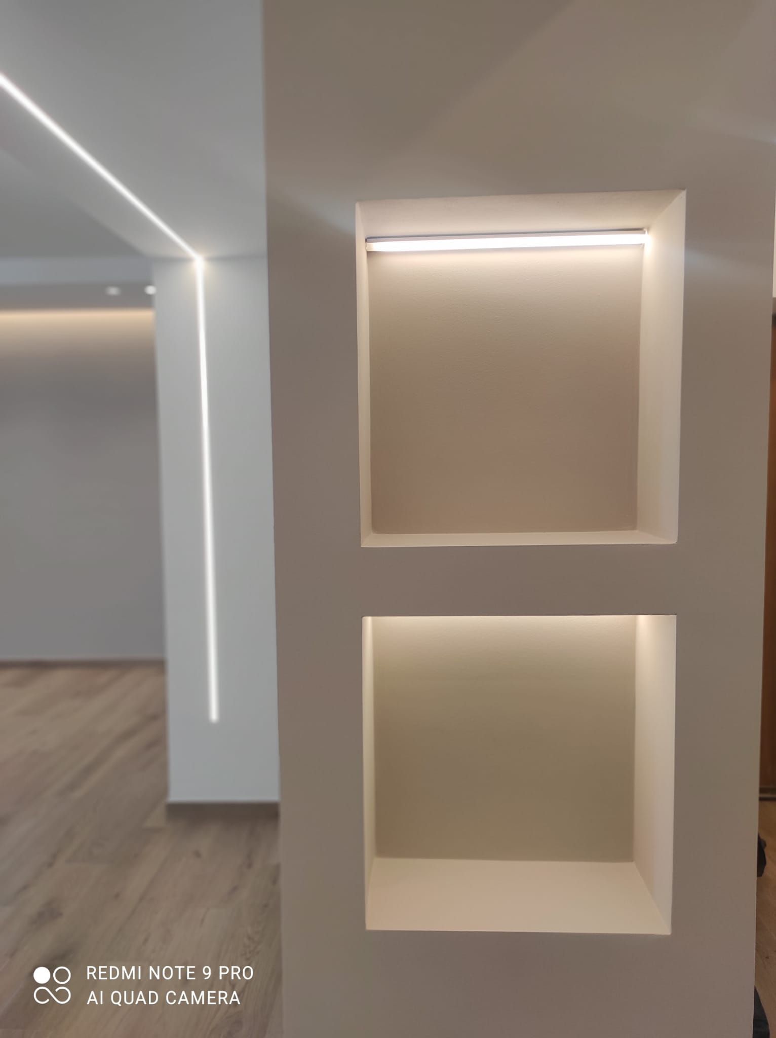 Nicchie a parete integrate illuminate da luci nascoste in un interno moderno, con luci lineari a soffitto e a parete.