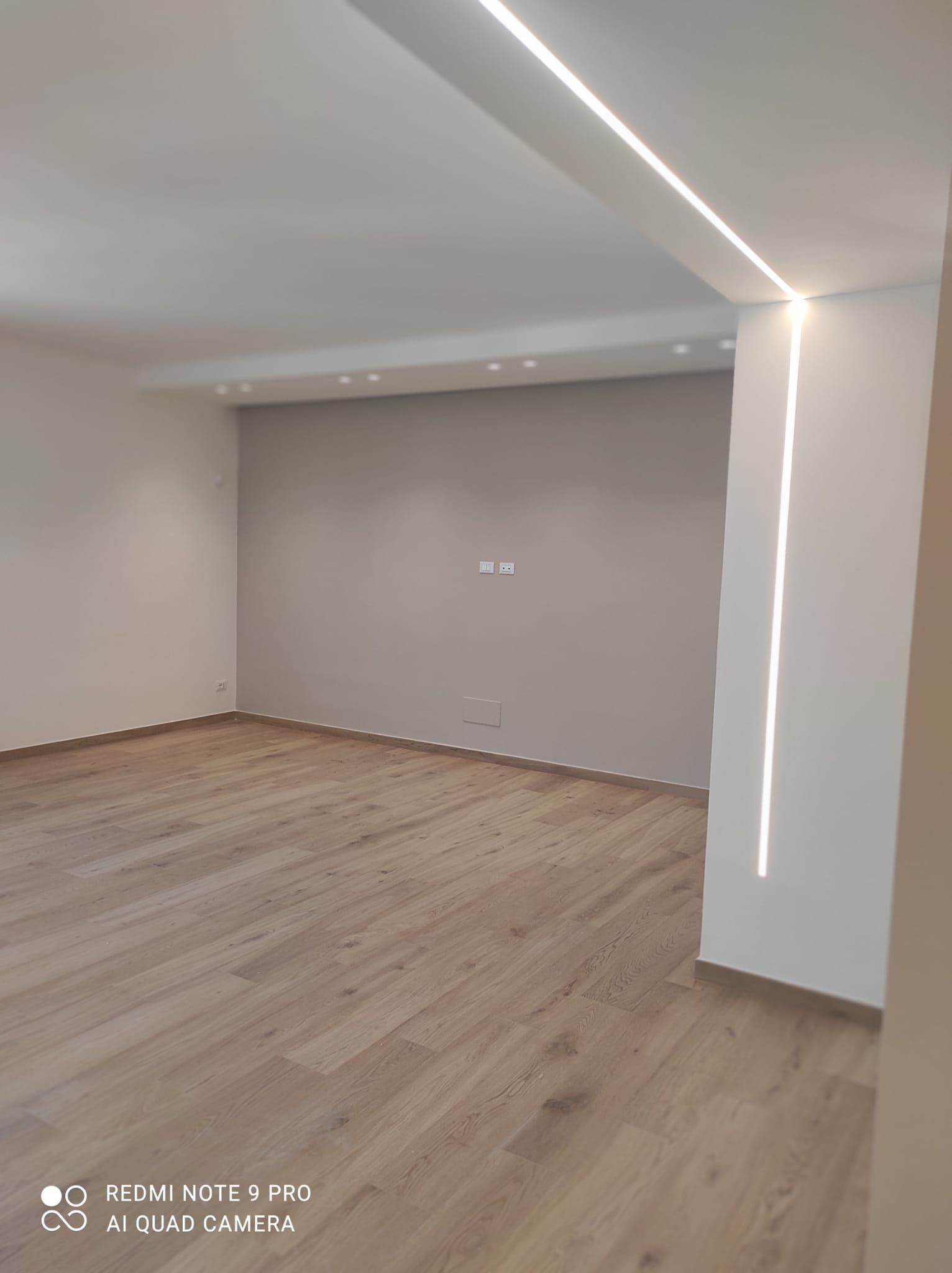 Stanza vuota con pavimenti in legno e illuminazione a incasso. Una striscia luminosa corre lungo il soffitto e le pareti.