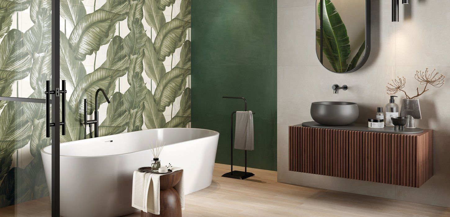 Bagno con vasca bianca, carta da parati a fantasia, mobiletto in legno con lavandino grigio e rubinetto nero.