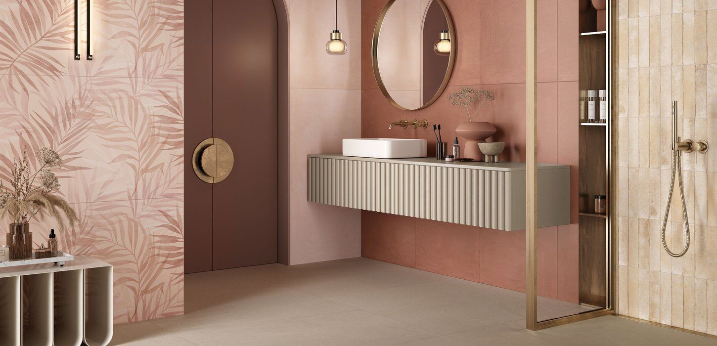 Elegante bagno con pareti rosa, porta marrone, pavimento beige, specchio rotondo e lavandino sospeso.